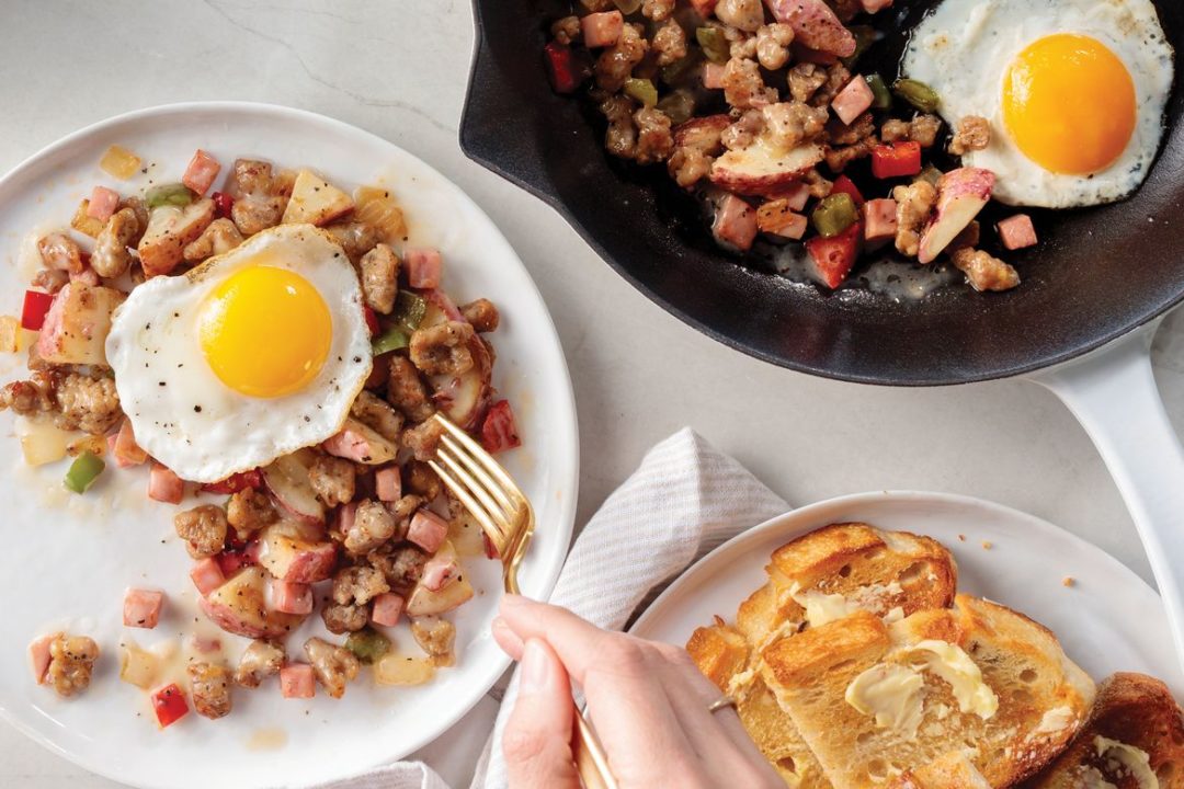 skillet breakfast with sunny side up egg on white plate. skillet and toast with butter in background