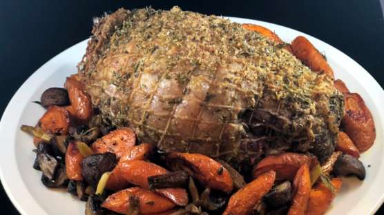 herbed boneless leg of lamb roast with purple and oranges carrots on white plate