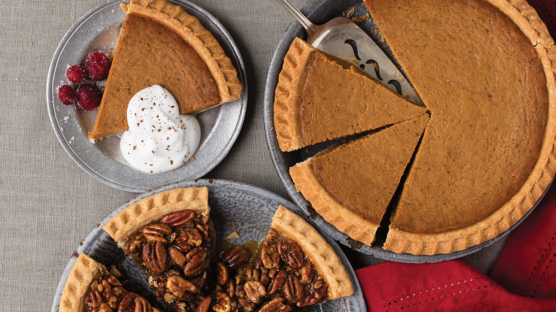 pumpkin pie in silver pie plate with one slice removed and plated on silver platter with creme, pecan pie in silver pie dish