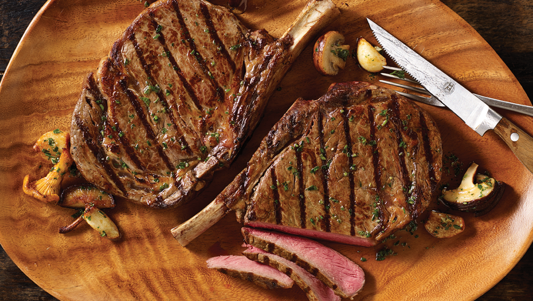 2 grilled cowboy steaks on platter with knife and fork