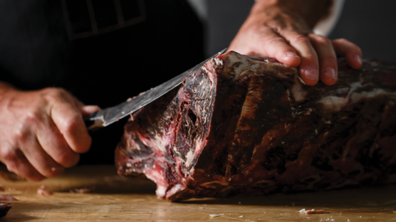 dry aged beef primal with butcher holding knife ready to trim edges