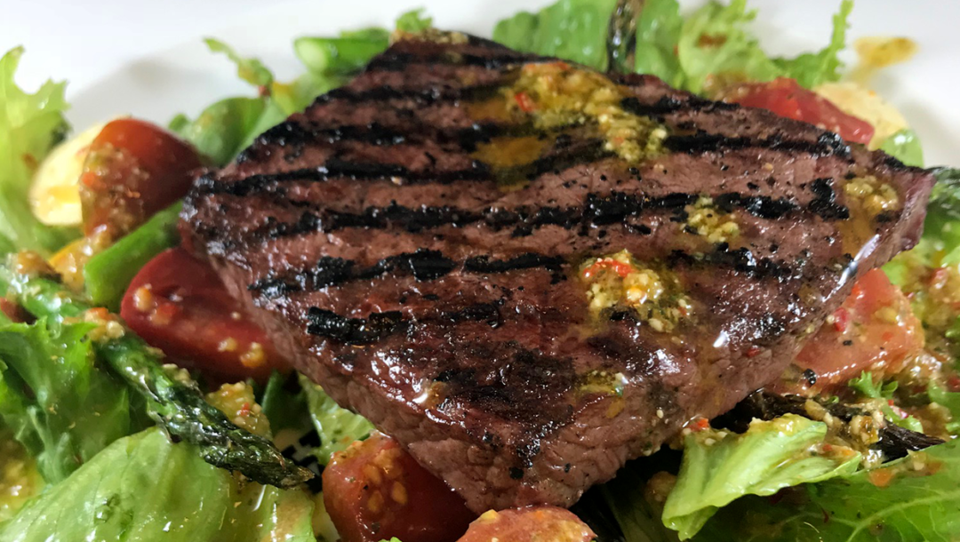 pesto salad topped with grilled flat iron steak on white plate