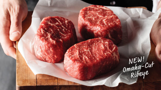 3 omaha cut ribeyes on butcher's paper on cutting board held by two hands