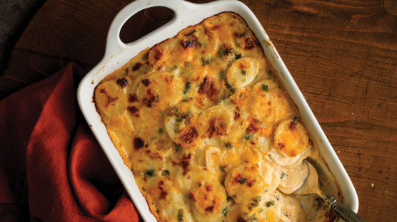 potatoes au gratin in white baking dish on wood table with red napkin