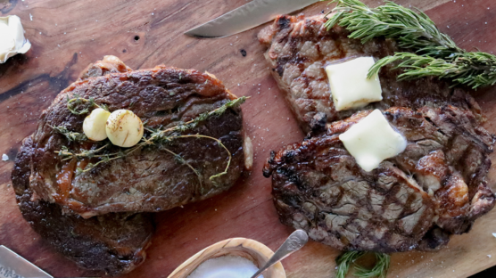 four cooked ribeyes on cutting board