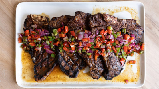 Four ancho chili rubbed porterhouse steaks with grilled onion and pepper salsa on a plate