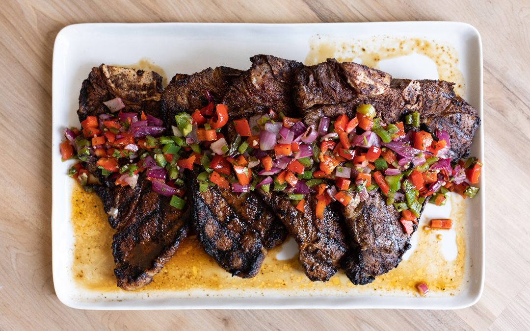 Four ancho chili rubbed porterhouse steaks with grilled onion and pepper salsa on a plate