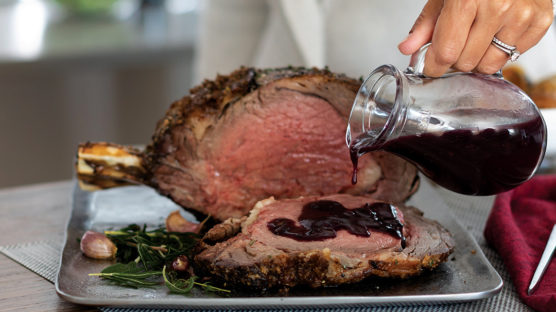 Pouring red wine sauce over sliced prime rib