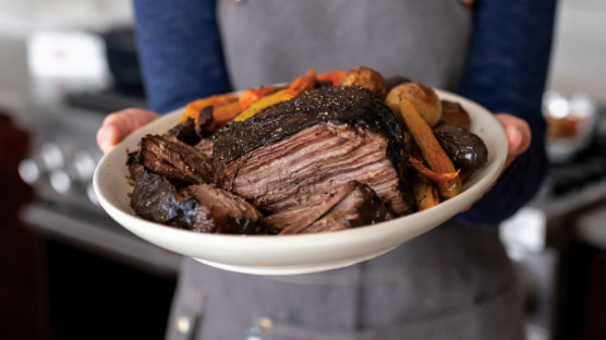 Woman holding a plate of cooked pot roast with carrots