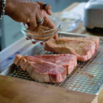 Seasoning two porterhouse steaks with an African spice rub blend