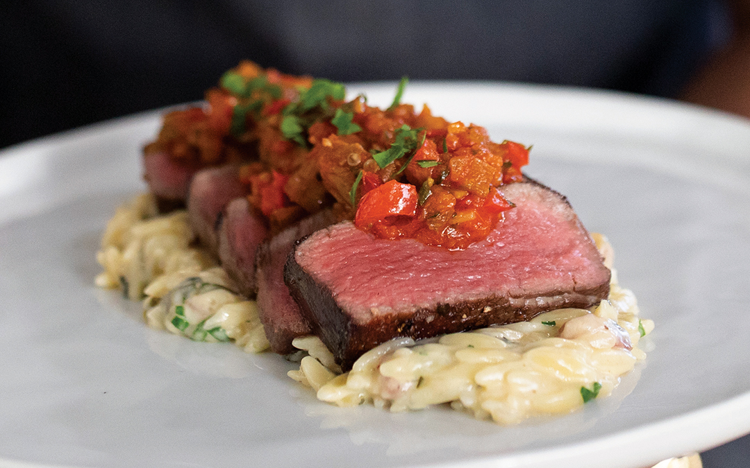 Reverse seared, medium-rare sliced filet mignon served with creamy orzo pasta with pancetta and topped with caponata