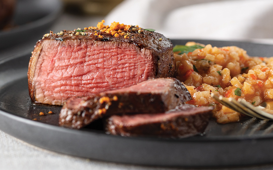 Suya-Dusted filet mignon sliced and cooked to medium-rare served with "red rice" risotto on a gray plate