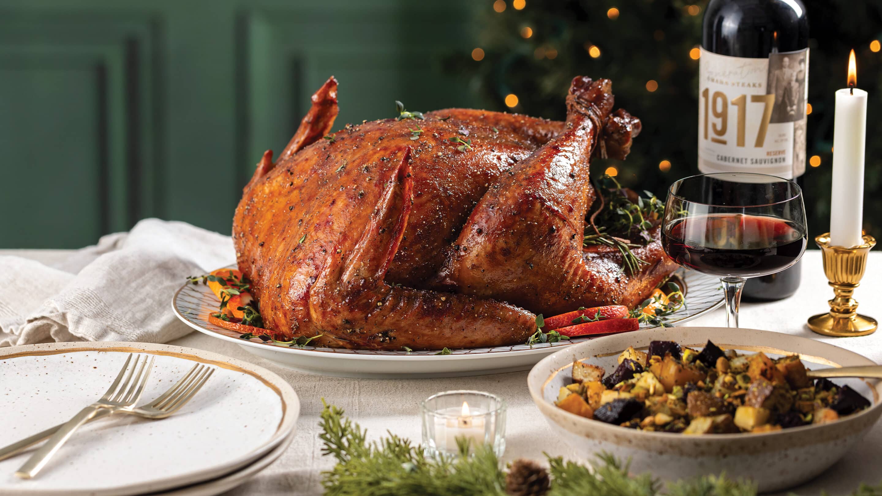 Holiday table set with sour cherry-cabernet glazed turkey, roasted root vegetables, and glass of Omaha Steaks 1917 cabernet wine.